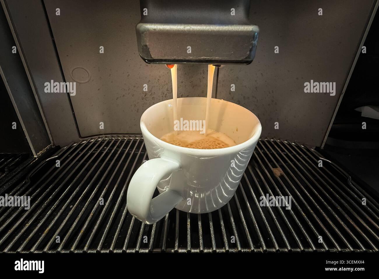 L'espresso si trasforma in una tazza bianca da una macchina da chicchi a tazze, mostrando due flussi e uno strato di crema sopra il vassoio antigoccia Il primo piano mette in risalto Foto Stock