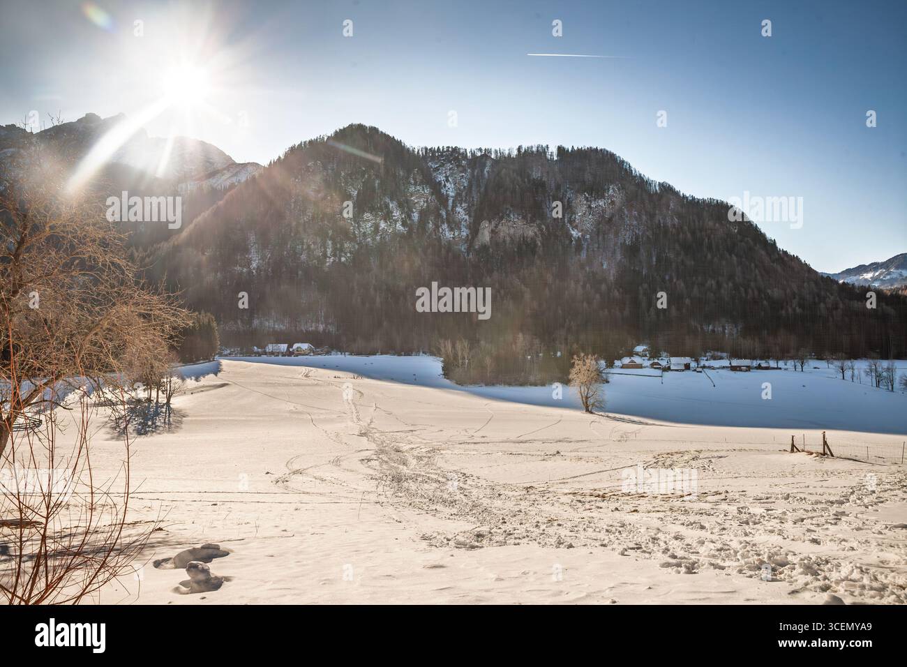 Ampia pianura innevata a Zgornje Jezersko, Slovenia, nelle Alpi Giulie. Il basso sole invernale proietta lunghe ombre e svela tracce sul prato bianco, con spirito Foto Stock