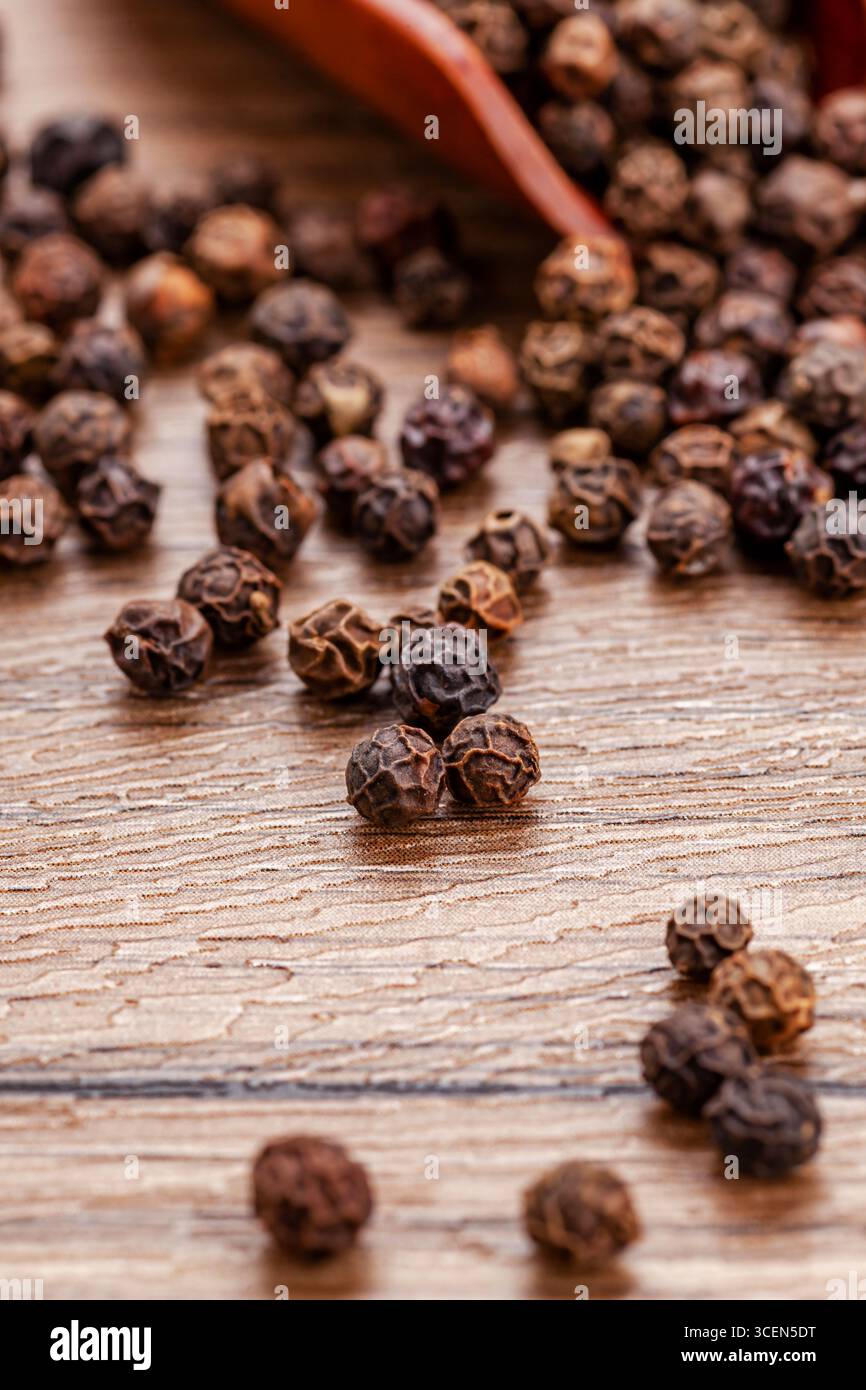 Grani di pepe nero su tavolo in legno con spazio copia - sfondo gastronomico rustico Foto Stock