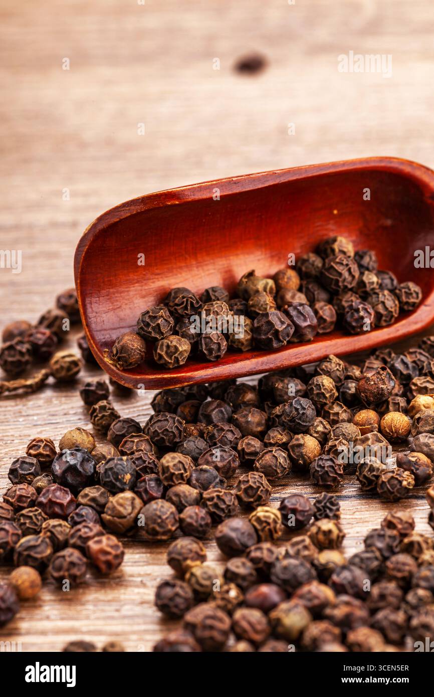 Grani di pepe neri in legno su tavola rustica - sfondo culinario verticale Macro Foto Stock
