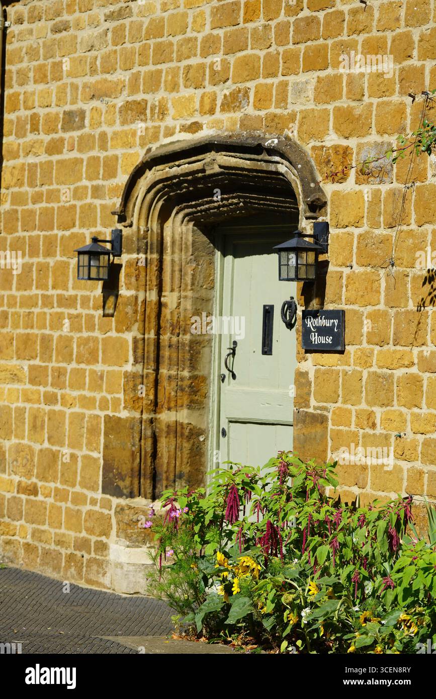 Affascinante casa in pietra con porta verde e fiori colorati in fiore. Deddington, Inghilterra Foto Stock