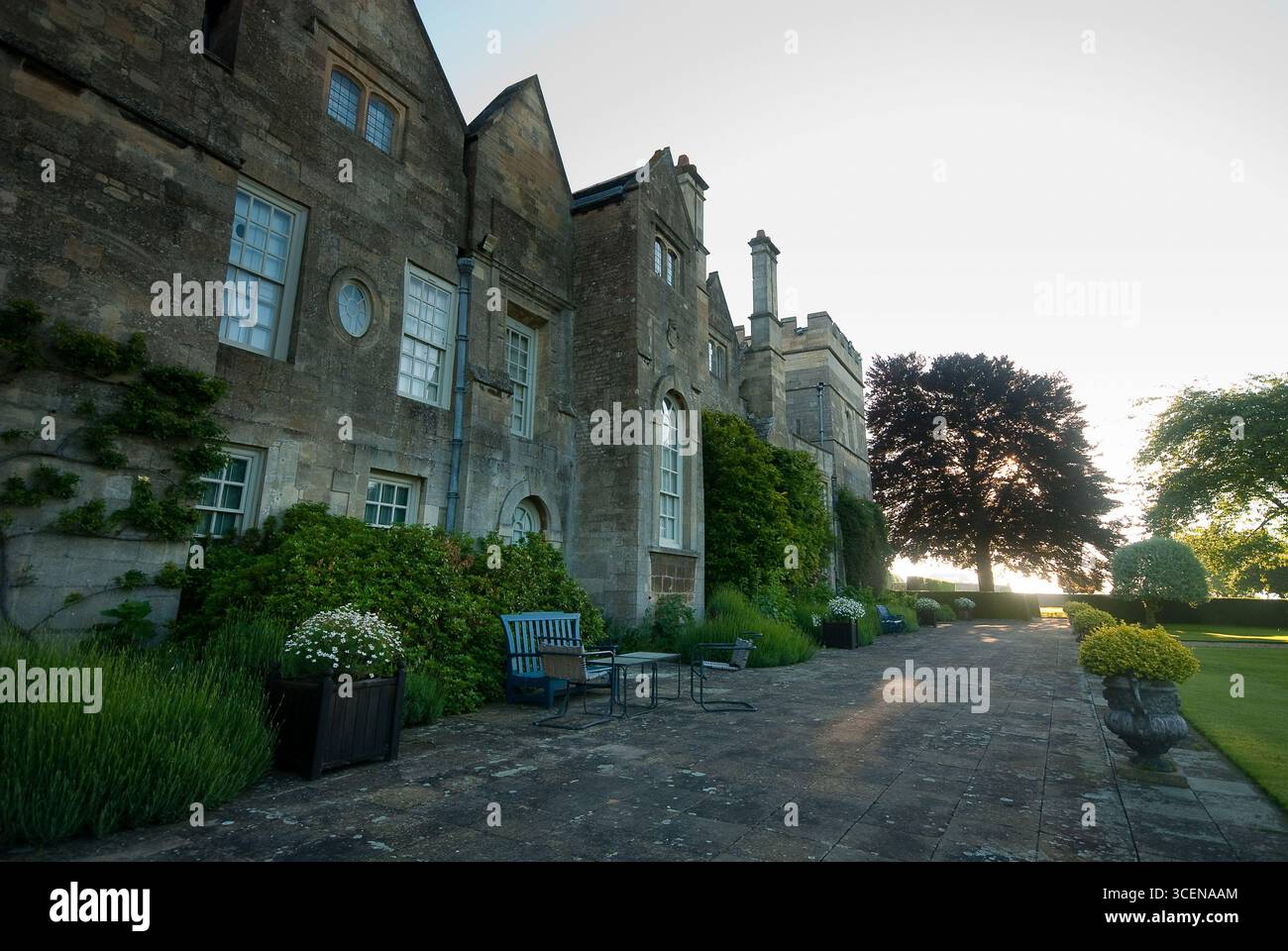 Una pittoresca vista di una casa padronale in pietra circondata da giardini ben tenuti, che mostrano posti a sedere all'aperto e una calda luce del tramonto. Foto Stock