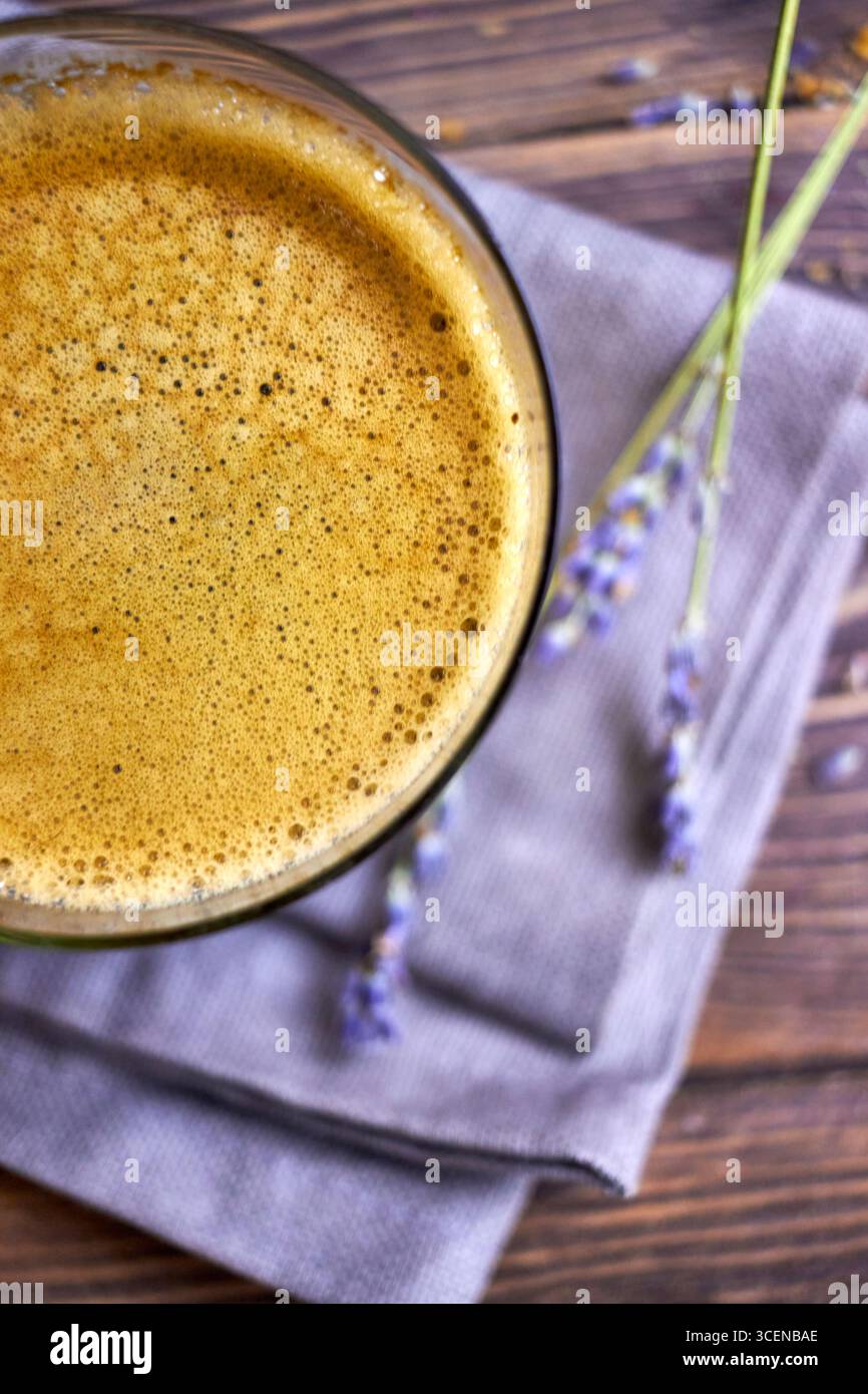 Primo piano del caffè appena preparato con schiuma cremosa, disegnato su un tavolo in legno rustico con accenti lavanda, perfetto per sfondi, marchi di caffè, e. Foto Stock
