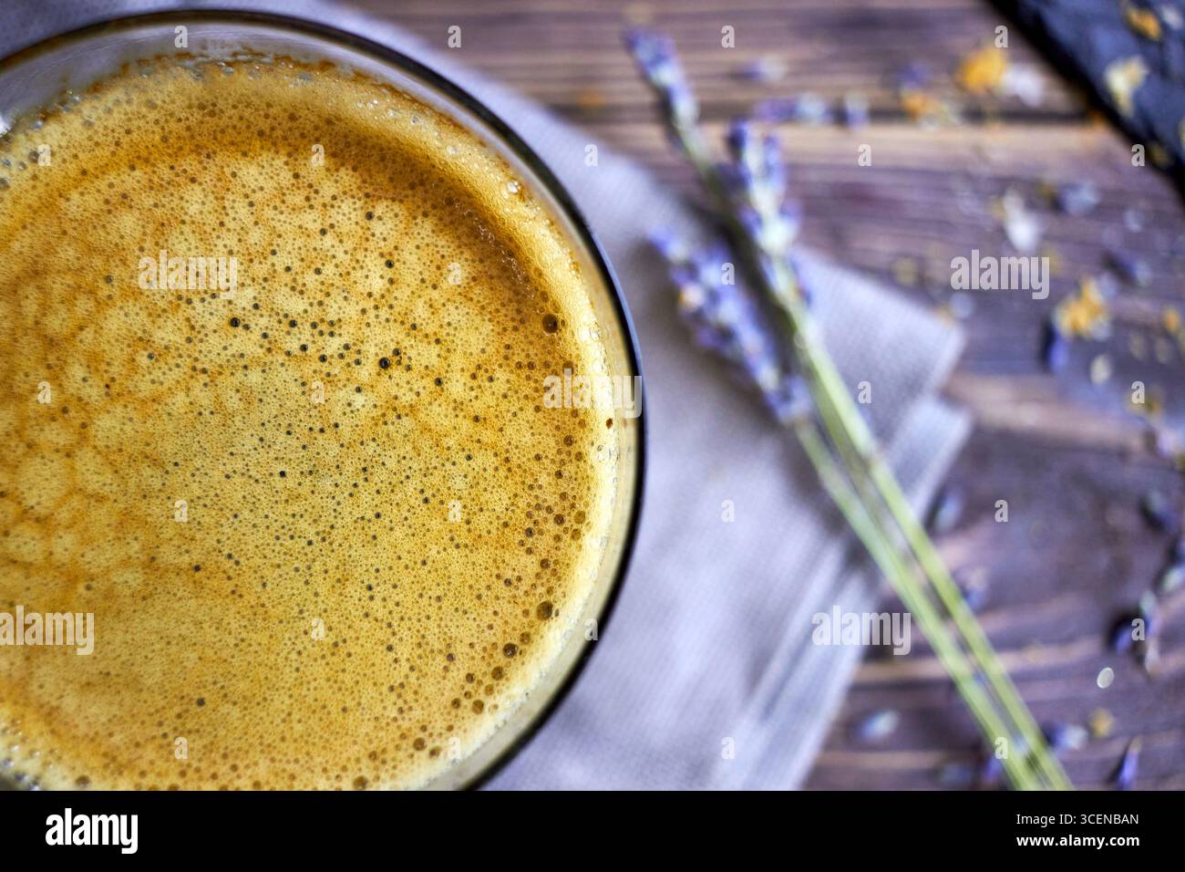 Primo piano del caffè appena preparato con schiuma cremosa, disegnato su un tavolo in legno rustico con accenti lavanda, perfetto per sfondi, marchi di caffè, e. Foto Stock