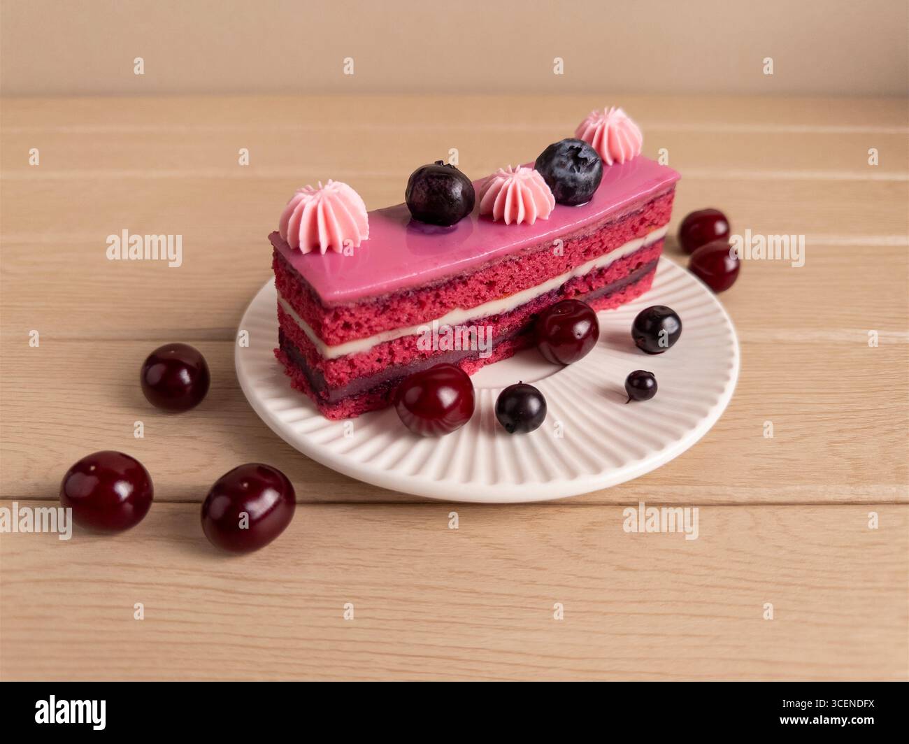 Una fetta di torta a strati splendidamente presentata con glassa rosa, decorata con mirtilli e bambole di panna rosa, posta su un piatto bianco. La torta Foto Stock