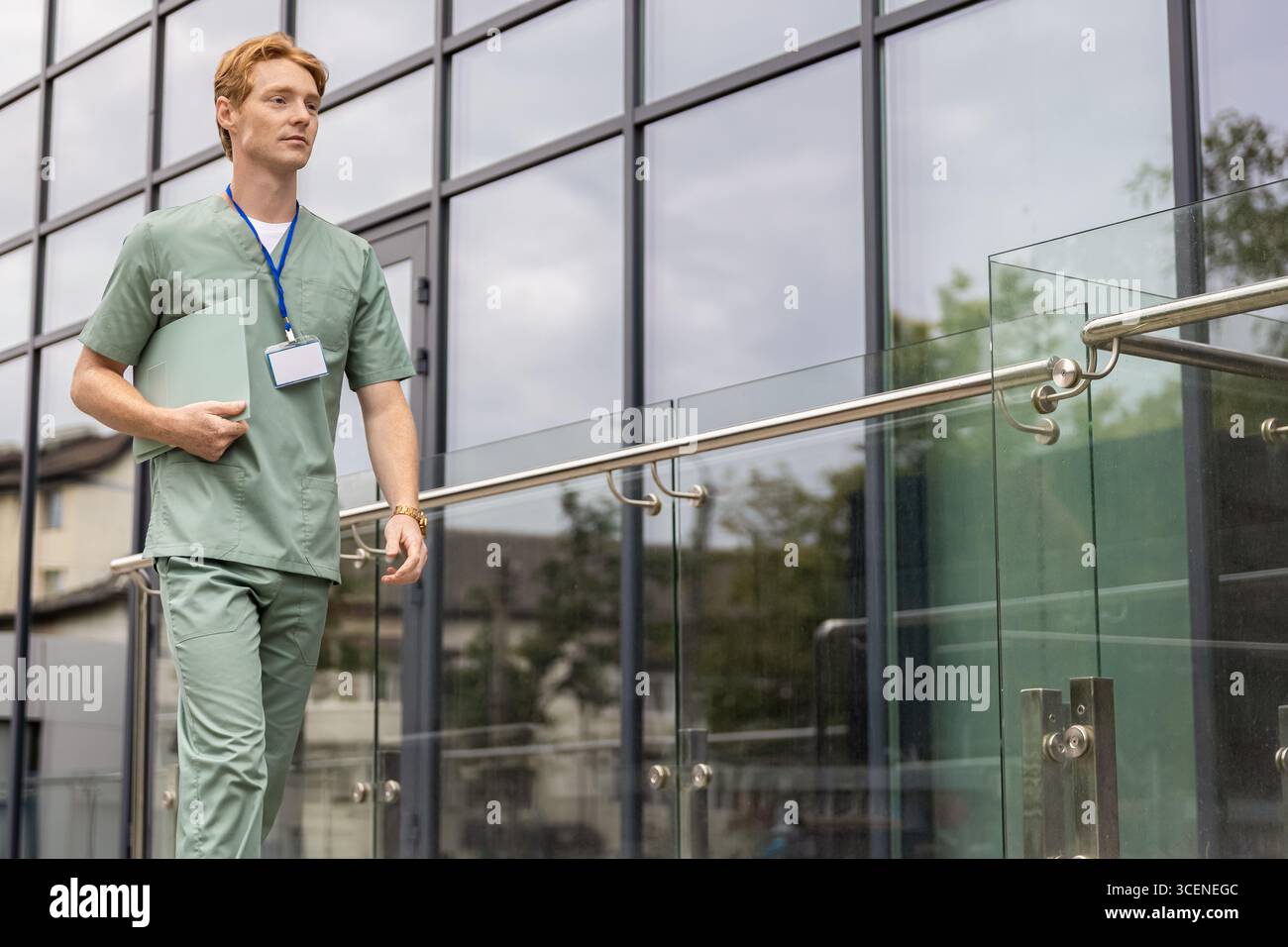 Zenzero medico in camice da laboratorio camminando in vetro clinica edificio tenendo cartella medica con storia clinica Foto Stock