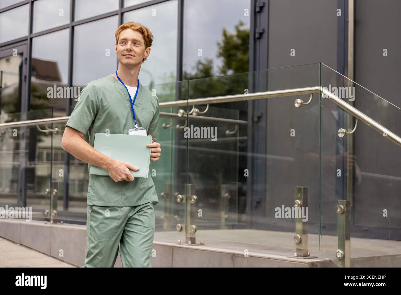 Zenzero medico in camice da laboratorio camminando in vetro clinica edificio tenendo cartella medica con storia clinica Foto Stock