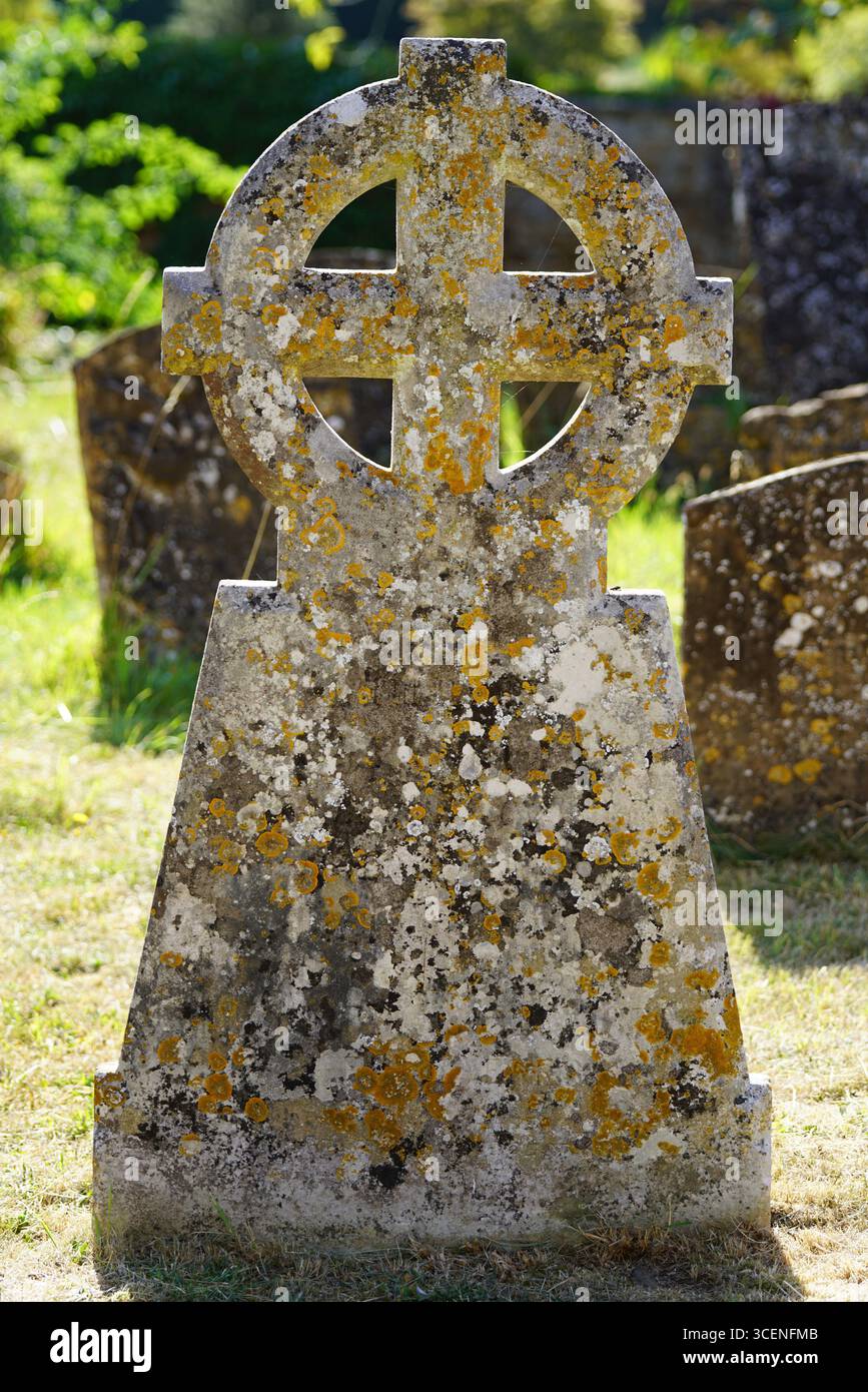 Lapide della Croce celtica intemprata in un cimitero verde illuminato dal sole. Adderbury, Inghilterra Foto Stock