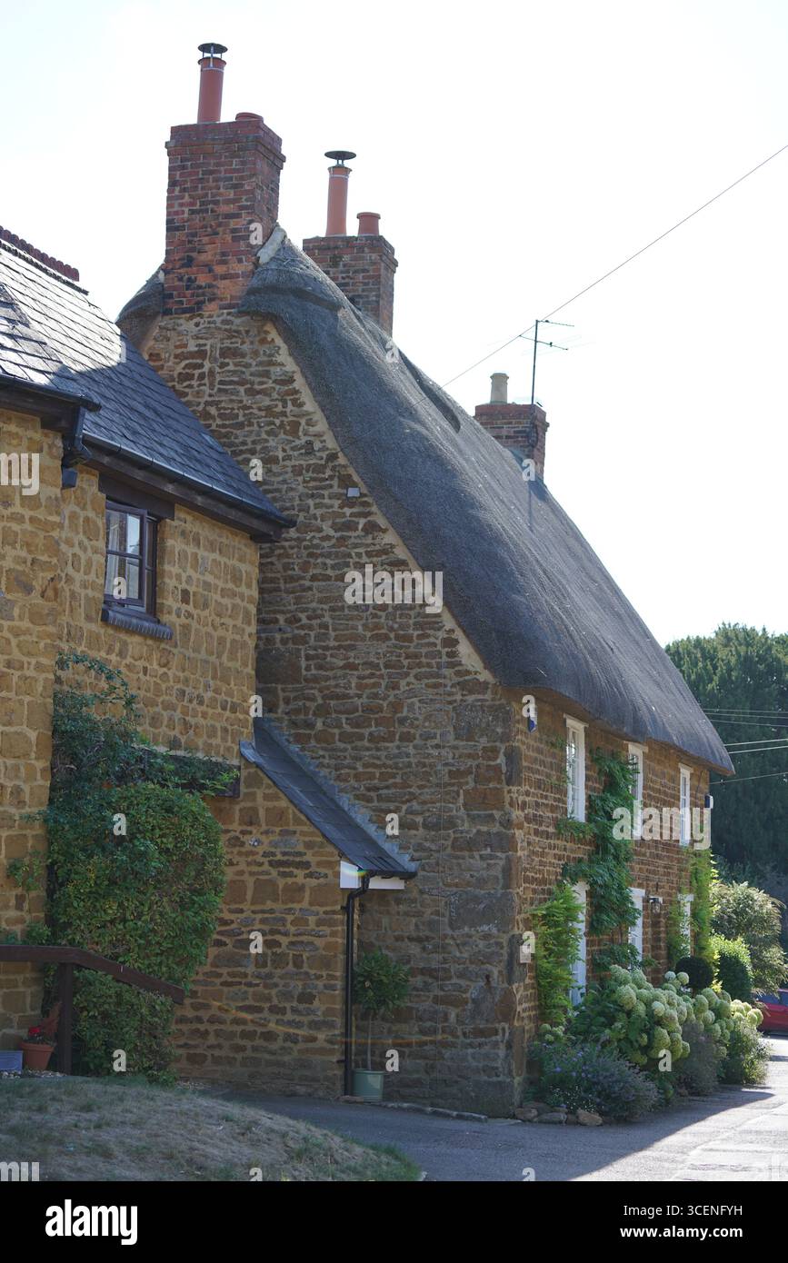 Cottage in pietra con tetto in paglia e vegetazione il giorno della soleggiata. Adderbury, Inghilterra Foto Stock