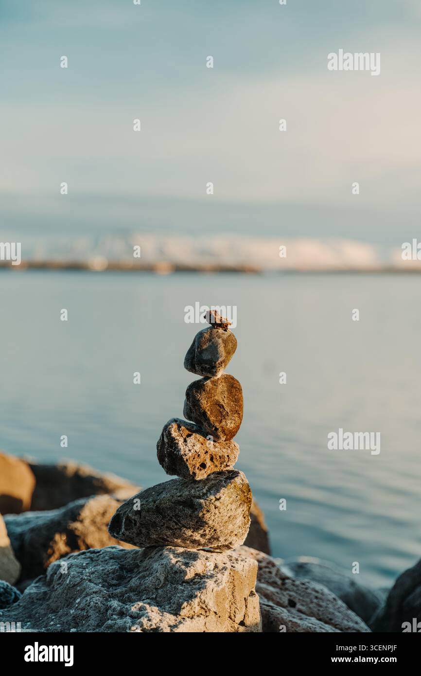 Cairne di pietra accanto a un fiordo innevato, Islanda occidentale, Islanda Foto Stock