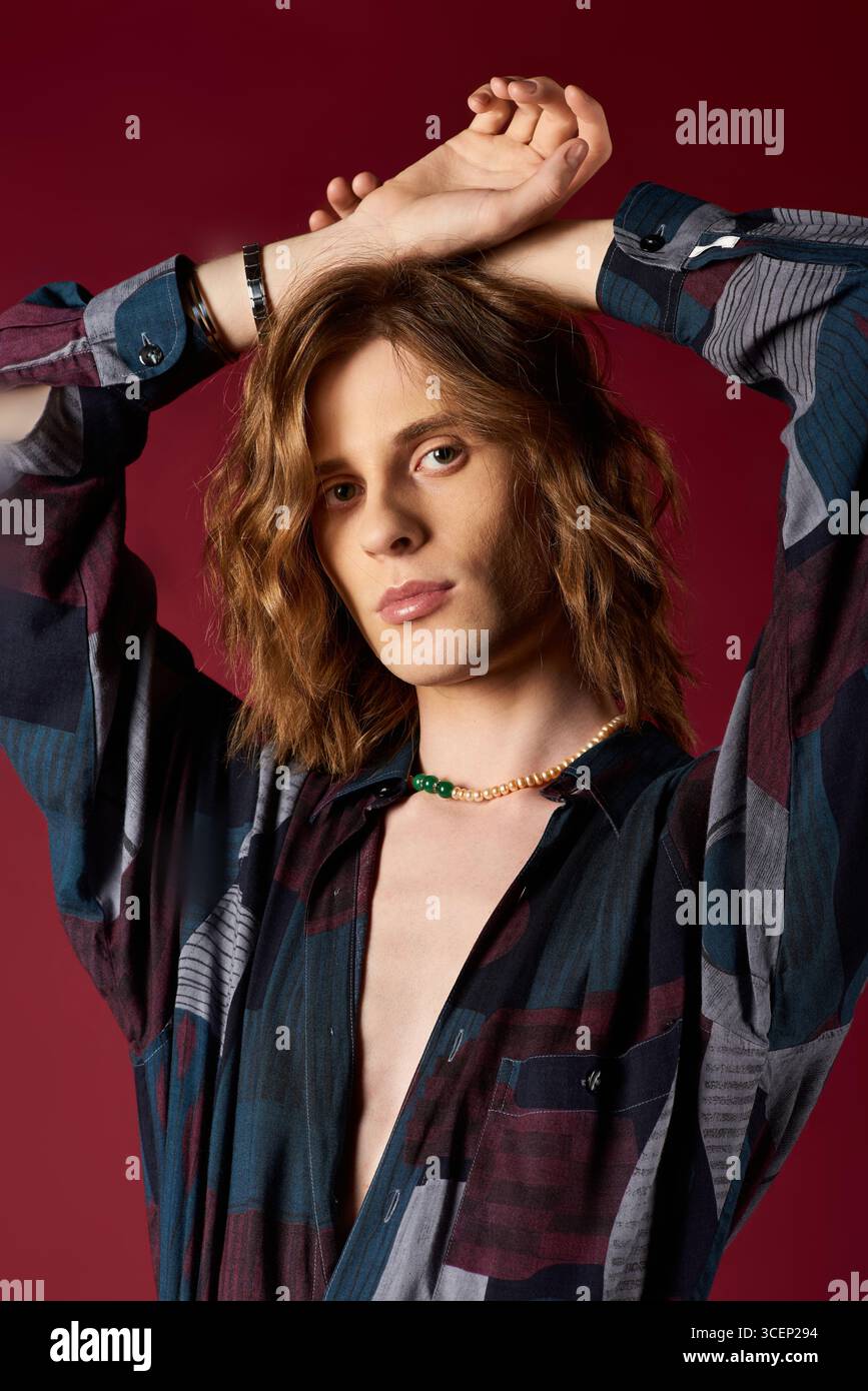 Un giovane uomo elegante con capelli lunghi indossa con sicurezza una camicia e accessori alla moda. Foto Stock