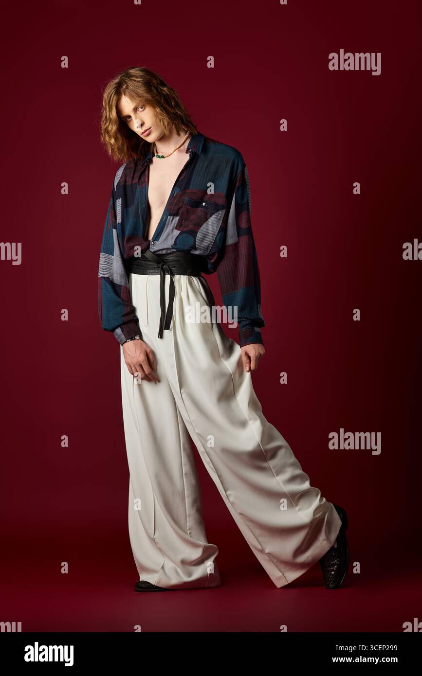 Un giovane uomo dal look femminile indossa elegantemente abiti vivaci su uno sfondo audace. Foto Stock