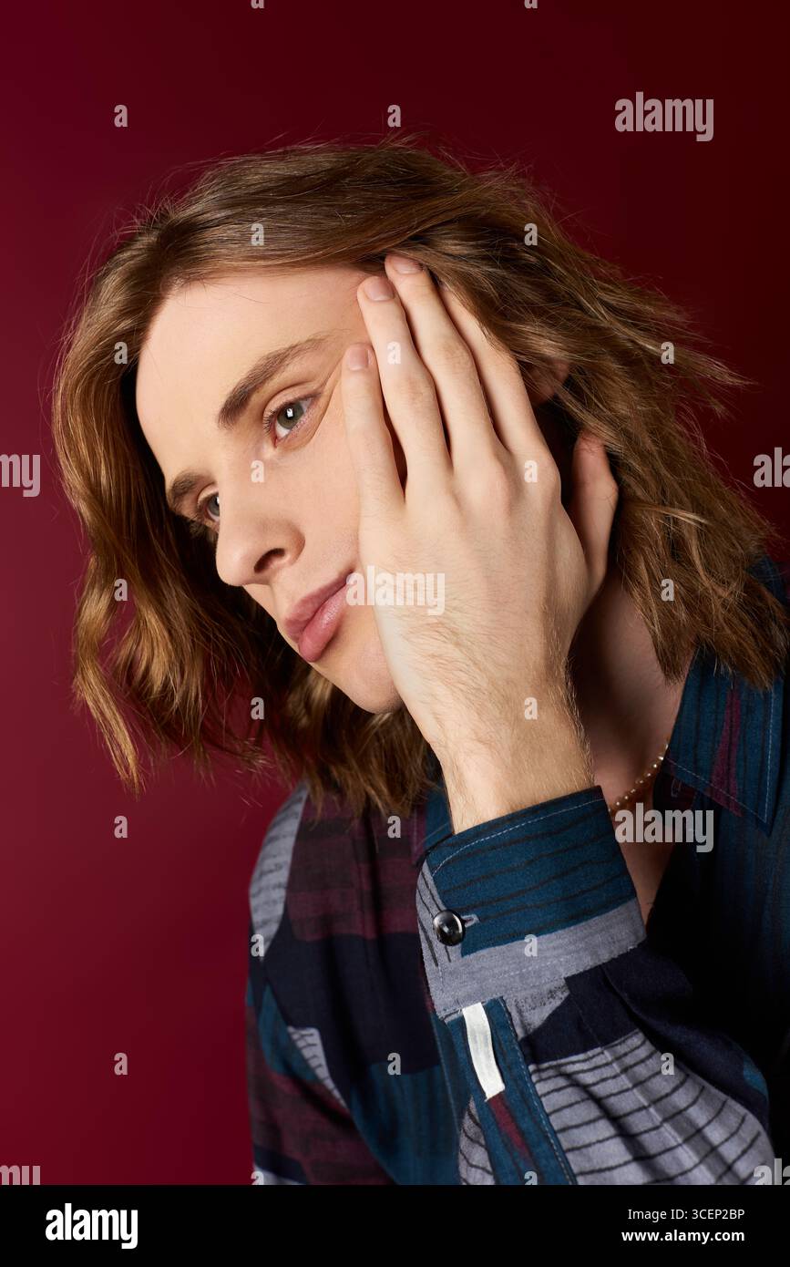 Un bel giovane uomo abbraccia il suo lato femminile con un outfit elegante e capelli ondulati, trasudando fascino. Foto Stock