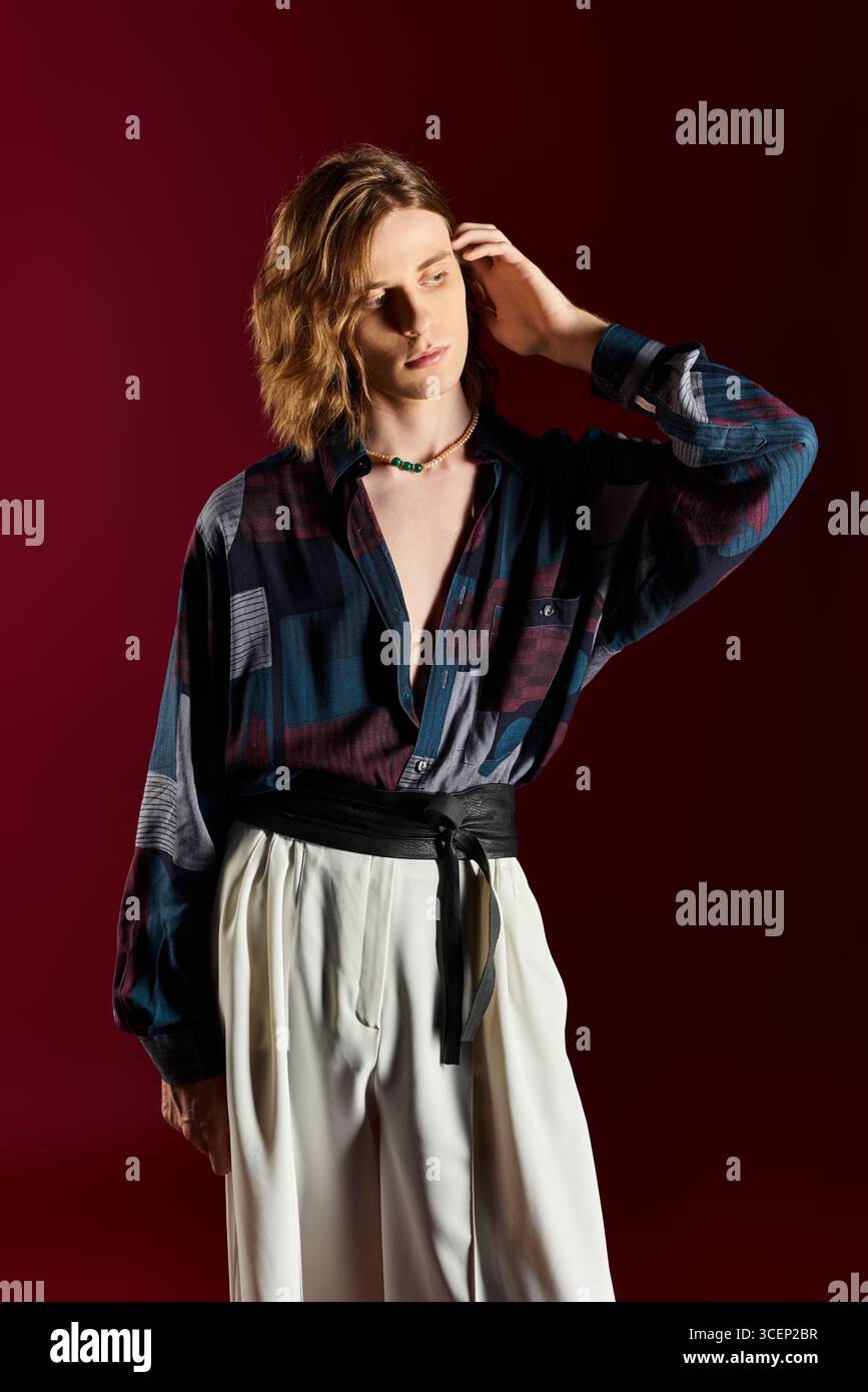 Un giovane uomo sfoggia uno stile elegante con un mix di elementi femminili e alla moda in una posa dinamica. Foto Stock