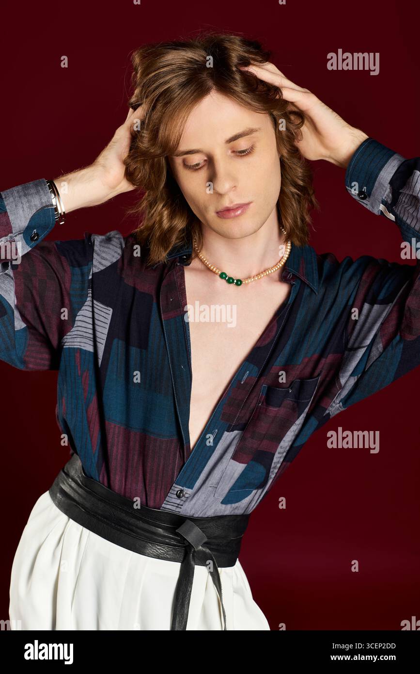 Un uomo giovane e bello sfoggia uno stile unico e femminile su uno sfondo rosso intenso. Foto Stock