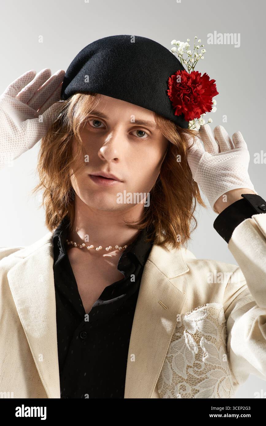 Un giovane uomo mette in mostra il suo stile unico in un outfit alla moda, regolando elegantemente un cappello. Foto Stock