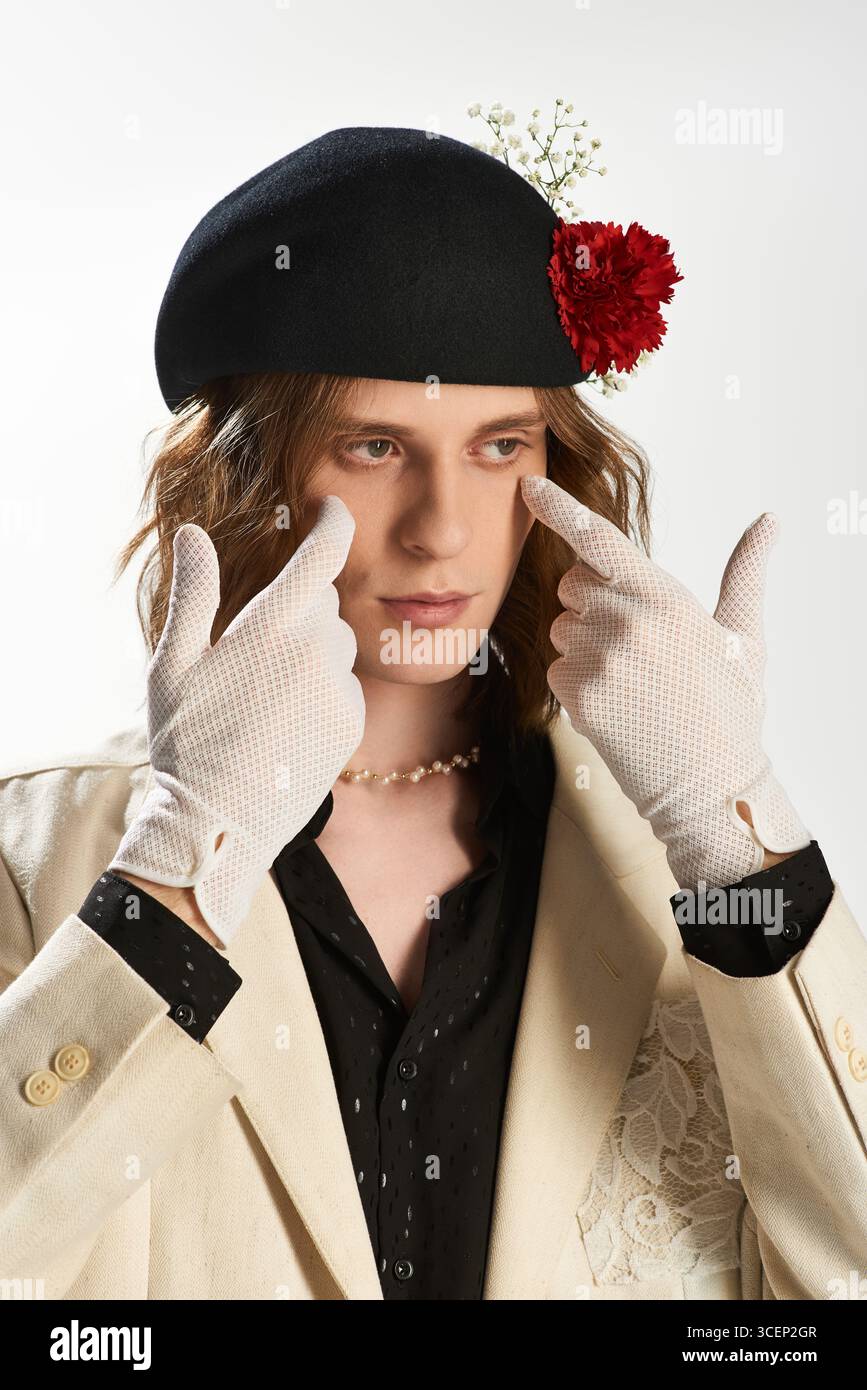 Un bel giovane uomo sfoggia il suo stile femminile con guanti e un cappello decorato con fiori. Foto Stock