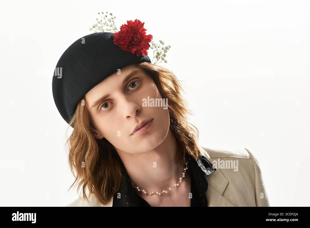 Un bel giovane uomo sfoggia un senso di moda unico con un accattivante cappello e dettagli floreali. Foto Stock