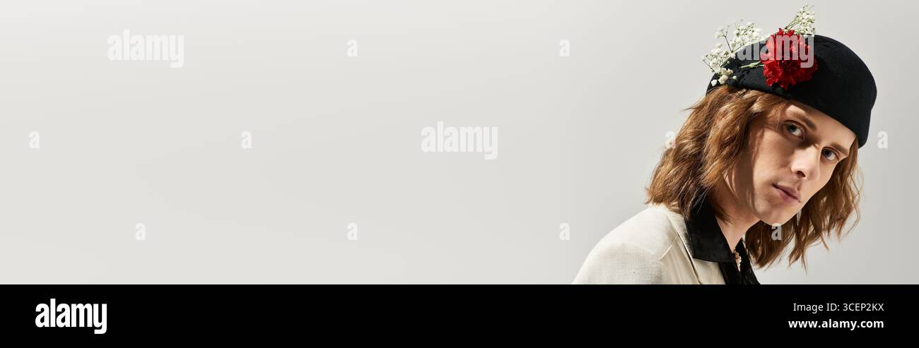 L'uomo femminile trasuda fascino e sicurezza, mentre presenta un abbigliamento alla moda decorato con fiori. Foto Stock