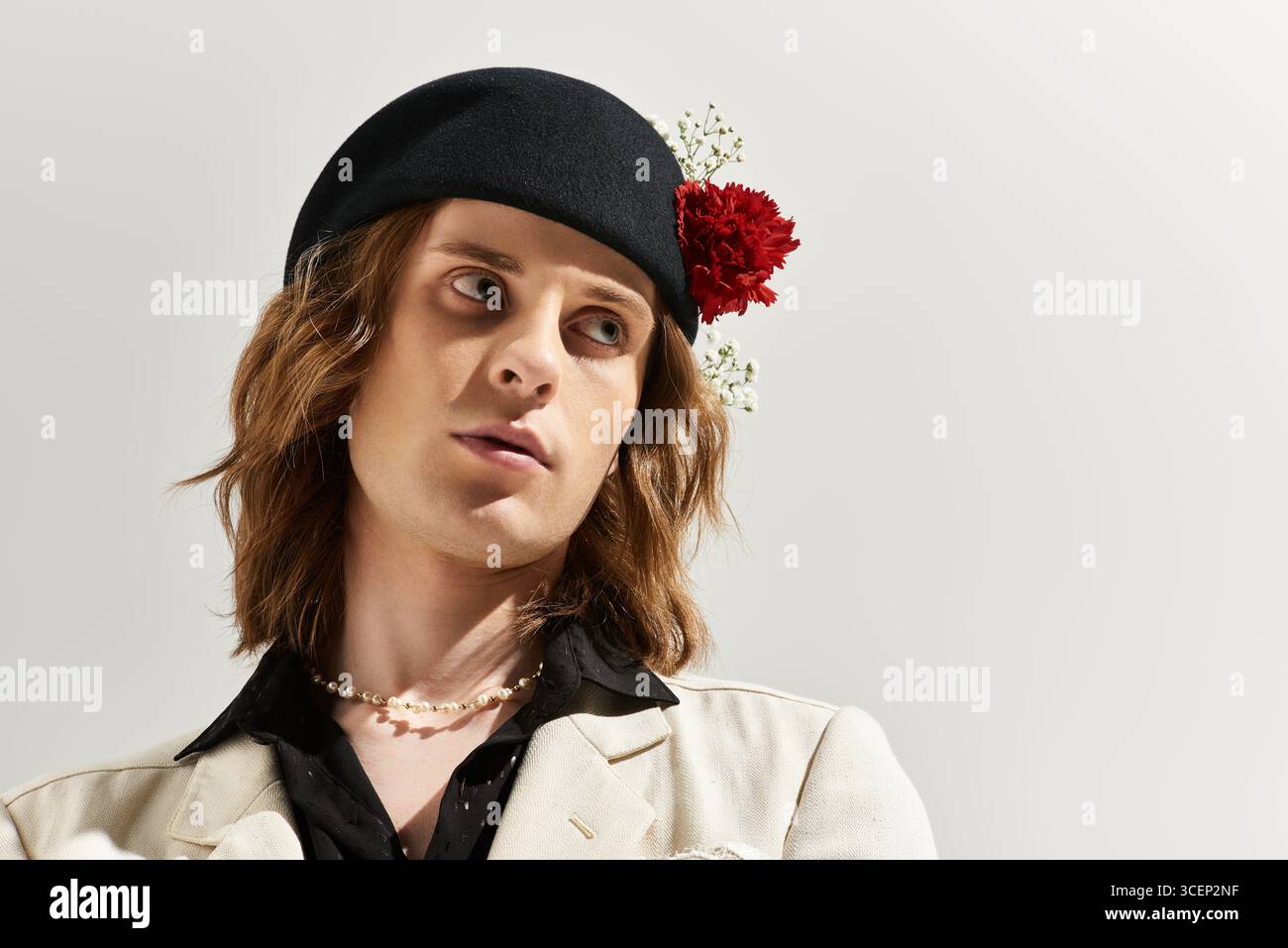 Un uomo giovane e bello presenta uno stile di moda unico con accenti floreali in un ambiente moderno. Foto Stock