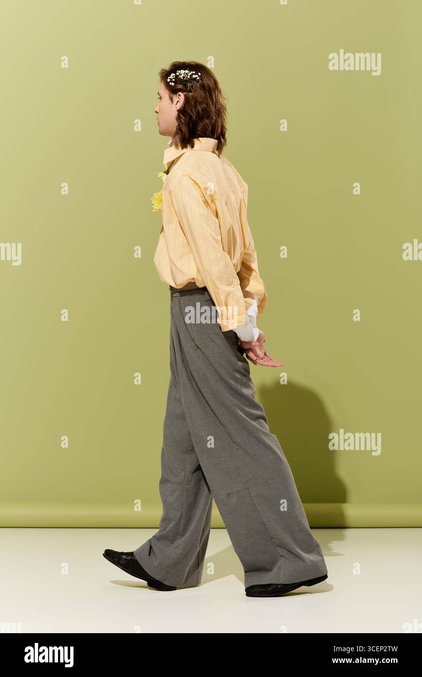 Un giovane uomo elegante sfoggia il suo look femminile su un morbido sfondo verde. Foto Stock
