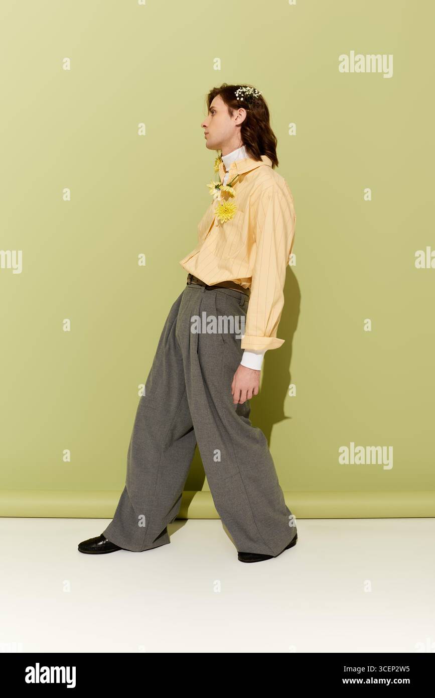 Un giovane uomo elegante dal look femminile si pone con sicurezza in un ambiente artistico. Foto Stock