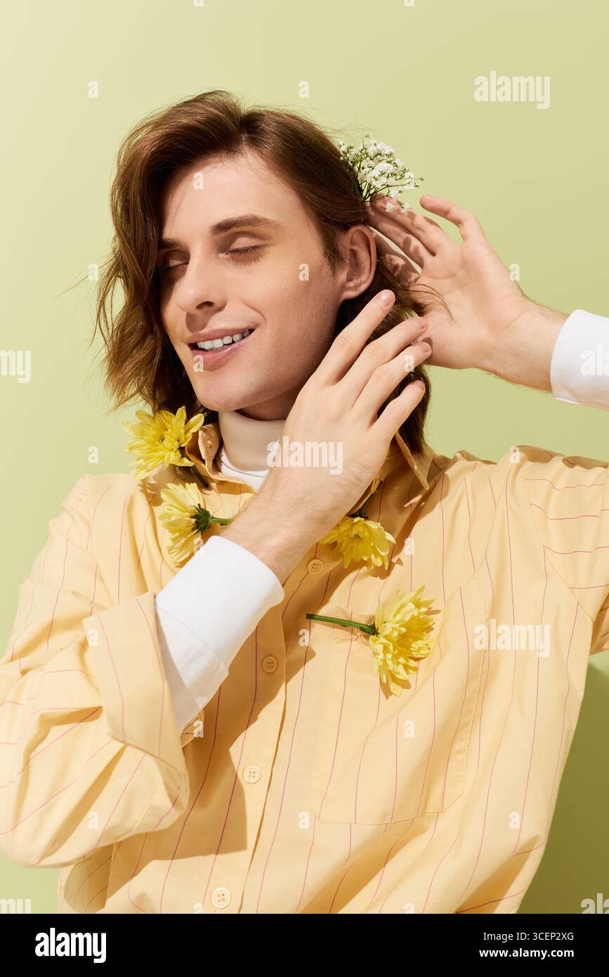 Il giovane uomo alla moda sfoggia il suo stile unico con dettagli floreali e fascino giocoso. Foto Stock