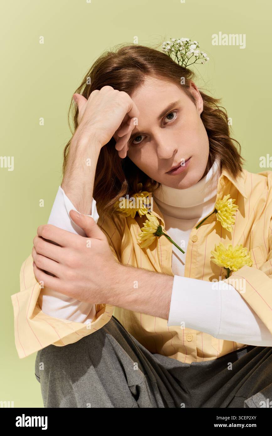 Un bel giovane uomo poggia con cura su uno sfondo verde tenue, mostrando il suo stile unico. Foto Stock