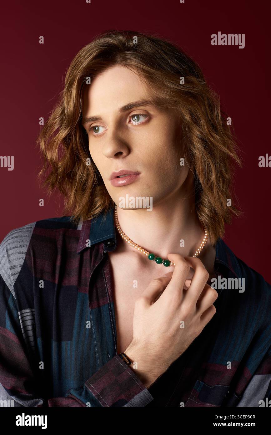 Un giovane uomo mostra il suo stile unico con una splendida collana su uno sfondo ricco. Foto Stock