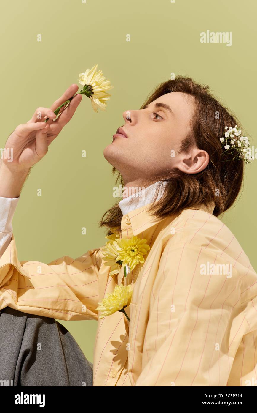 Un bel giovane con uno stile unico interagisce dolcemente con i fiori in un ambiente morbido. Foto Stock