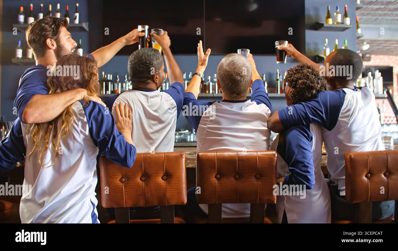 Vista posteriore degli amici che indossano i colori della squadra mentre guardano la partita al bar dello sport festeggiando Foto Stock