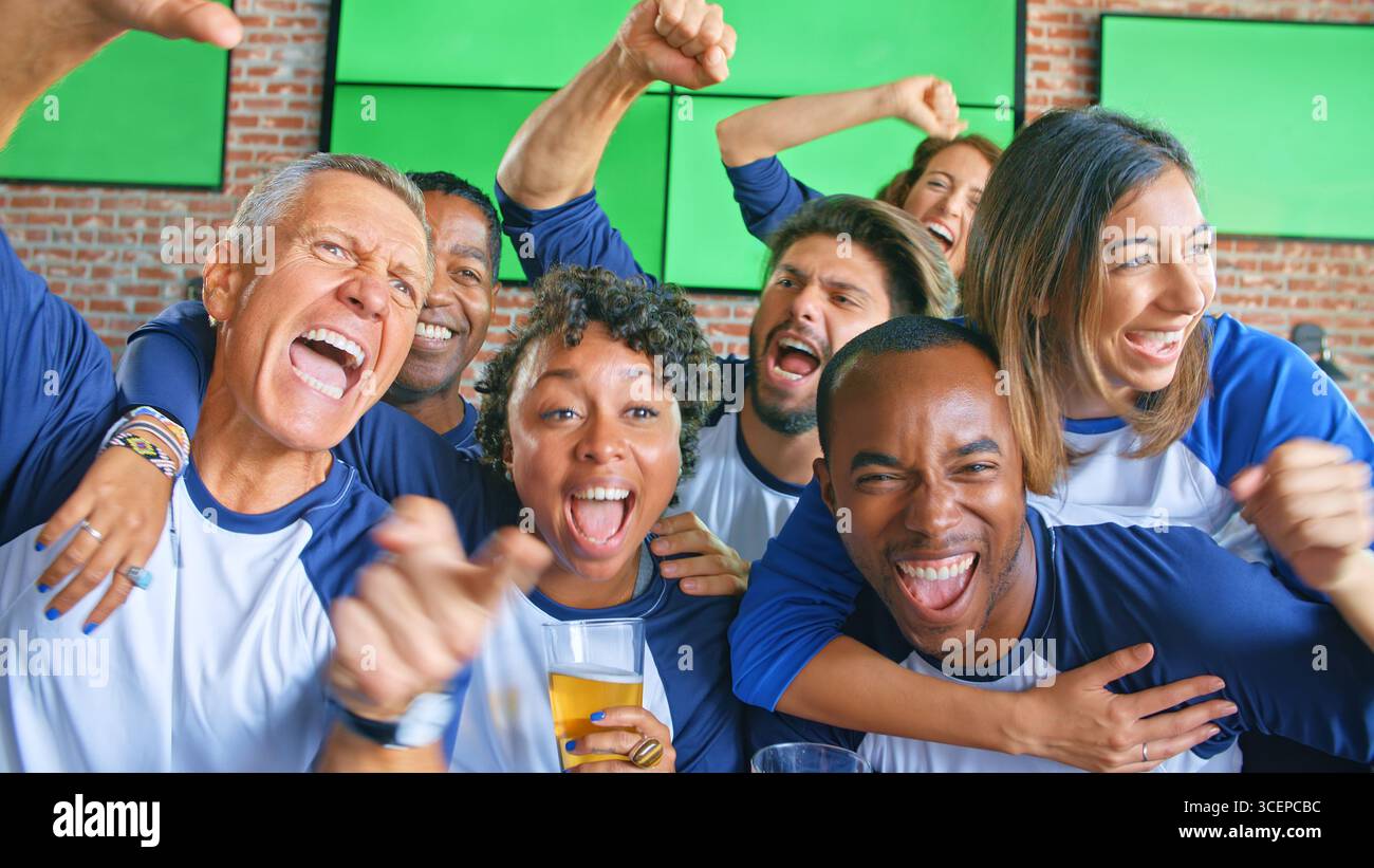 Amici multiculturali entusiasti che indossano i colori della squadra guardando la partita nella barra dello sport sugli schermi Foto Stock
