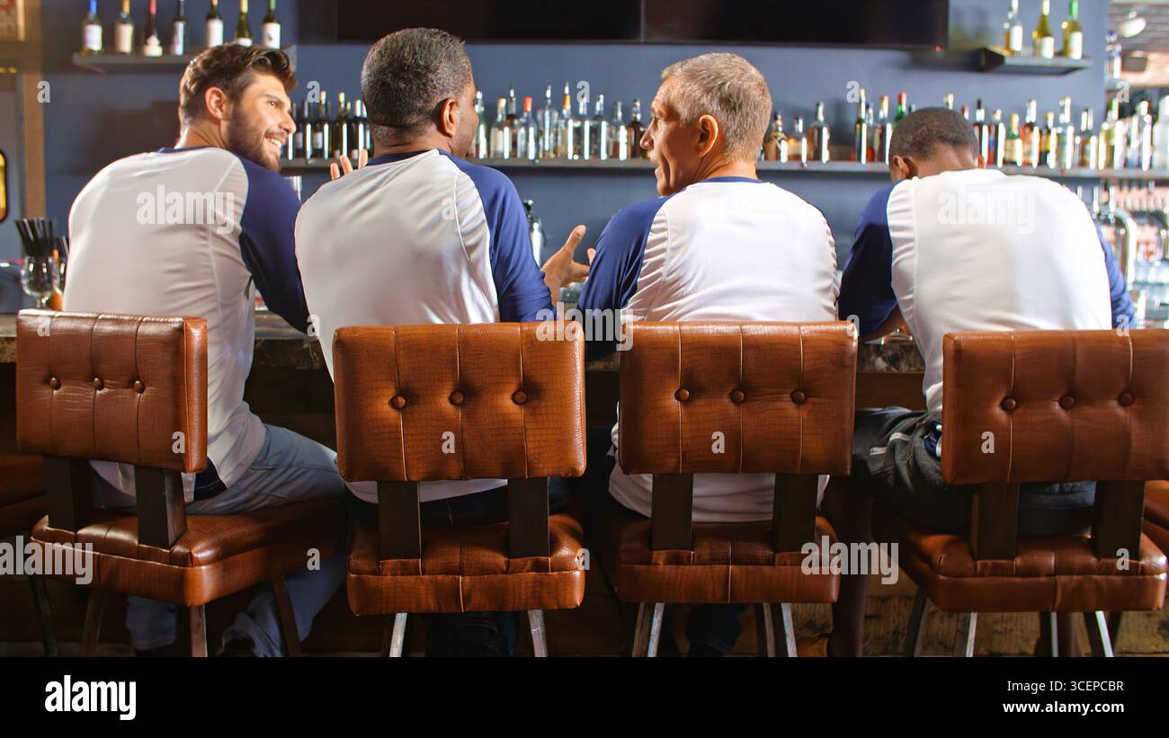 Vista posteriore degli amici maschi che indossano i colori della squadra mentre guardano la partita nel bar dello sport Foto Stock