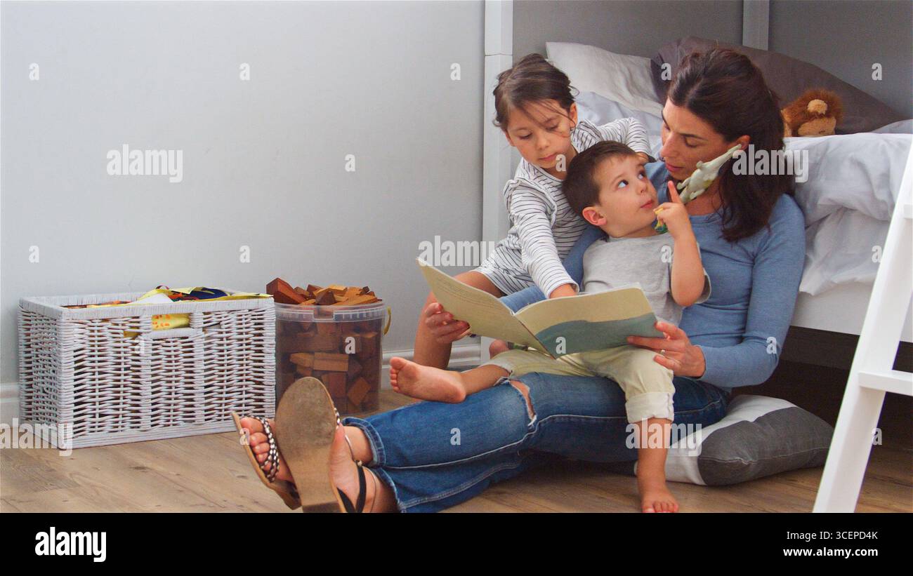 Madre seduta sul pavimento che legge la storia ai bambini nella loro camera da letto a casa Foto Stock