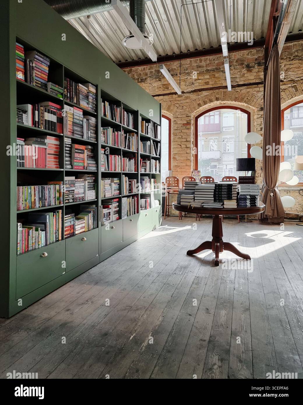Sala biblioteca con libri. Scaffale verde in una libreria in un vecchio edificio con pareti in mattoni e pavimenti in legno duro. Foto Stock