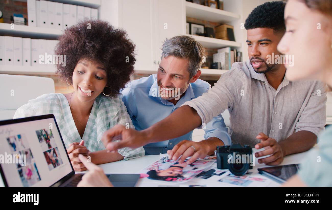 Team creativo multiculturale con riunione portatile che esamina i layout Foto Stock