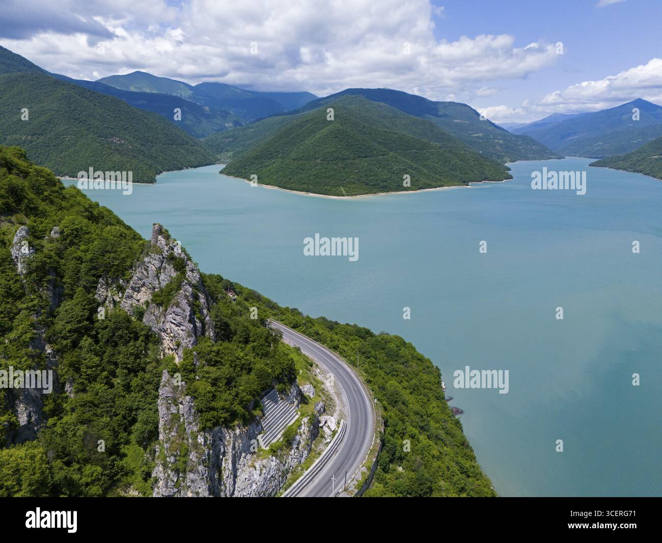 La strada tortuosa conduce lungo un lago circondato da montagne sotto un cielo blu nuvoloso, vista aerea, bacino idrico di Zhinvali, Shinvali, Jinvali o Shinvali, Mtskh Foto Stock