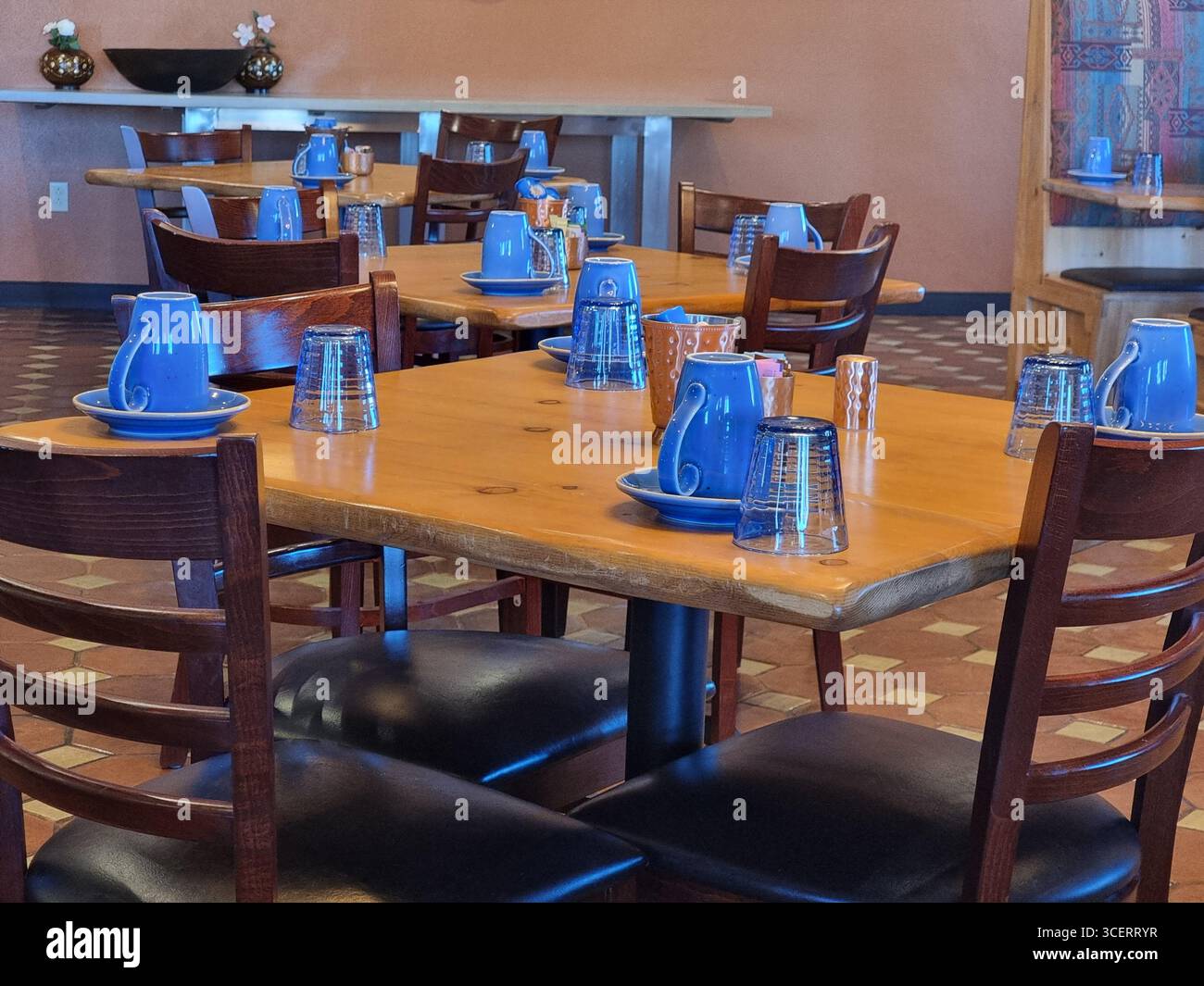 Tazze/tazze da caffè di colore blu brillante su tavoli di legno con sedie di legno; interno del ristorante in stile New Mexican all'ora della colazione Foto Stock