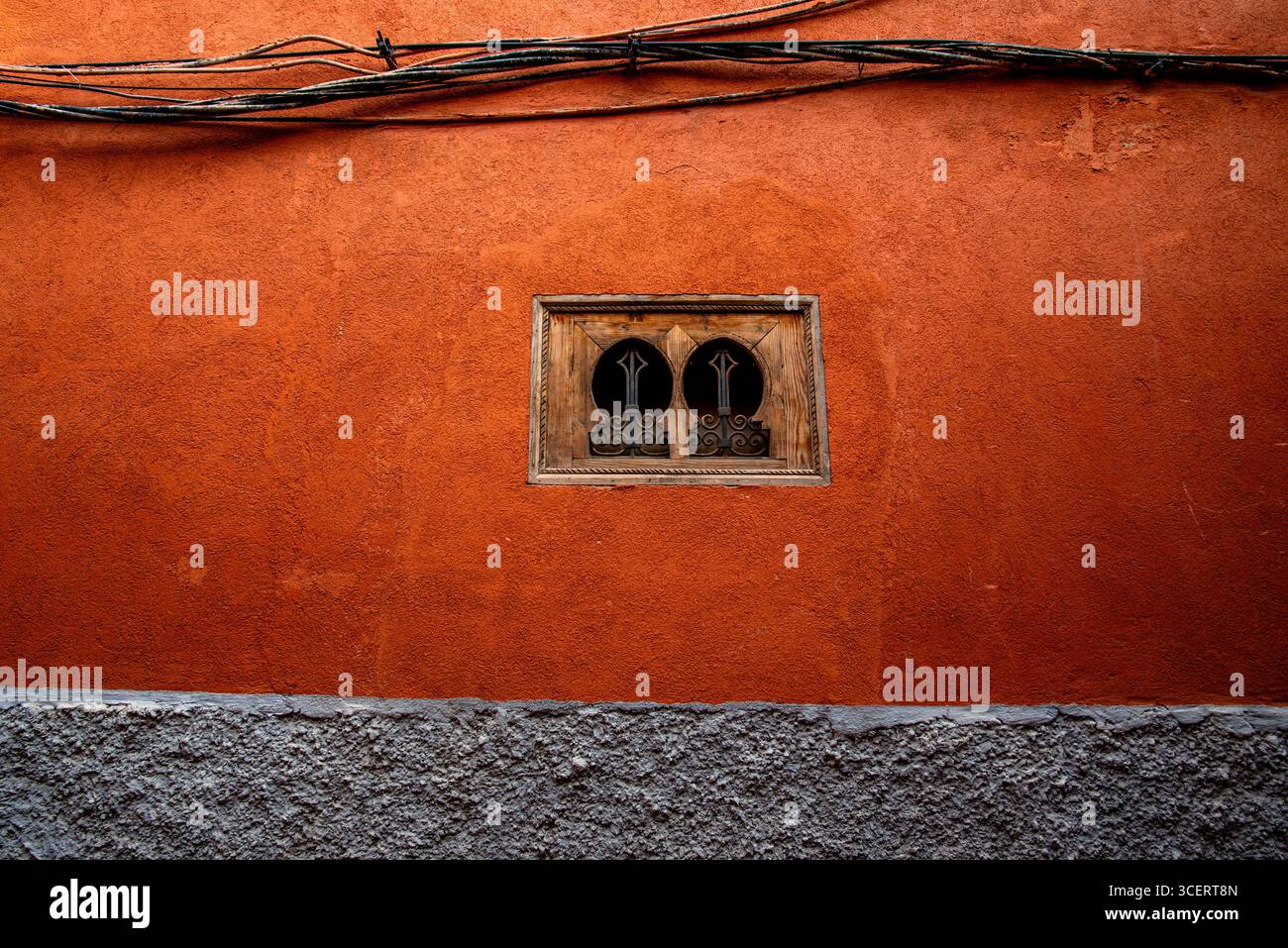 Una parete rustica arancione caratterizzata da una finestra in legno dal design complesso e fili elettrici esposti, che mostrano una miscela di texture e colori in urban Foto Stock