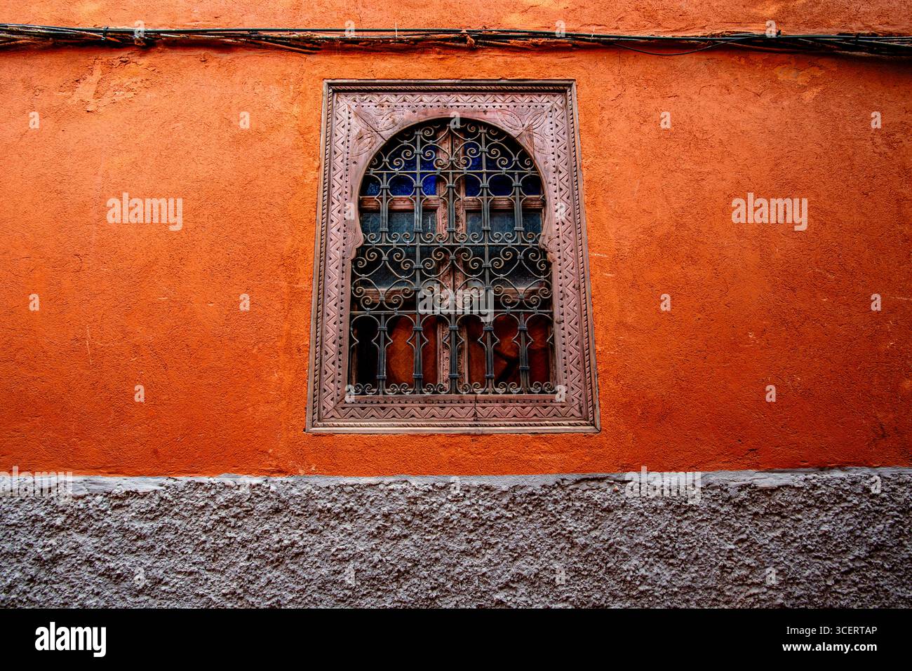 Intricato design delle finestre adagiato su una vivace parete arancione, che mostra la tradizionale architettura e artigianato marocchino. Foto Stock