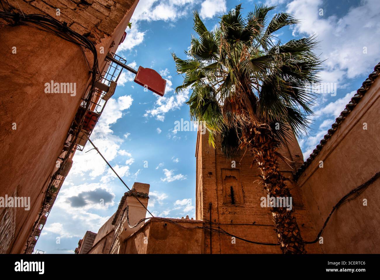 Vicolo tradizionale a Marrakech, Marocco, con pareti di argilla, palme e un cielo azzurro. Una vista panoramica del patrimonio urbano mescolando cultura, architec Foto Stock