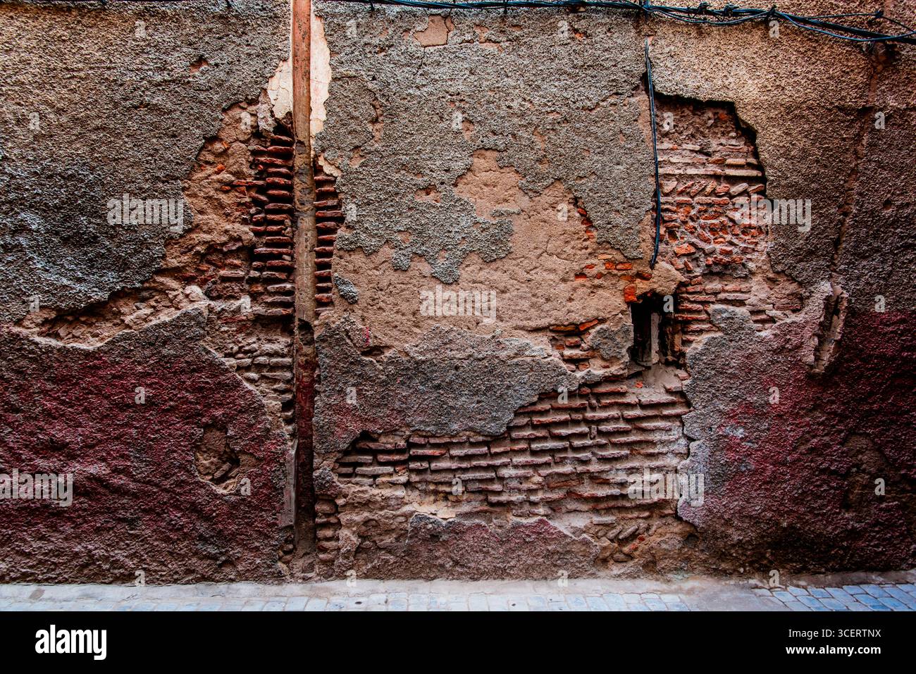 Pareti intemprate a Marrakech, Marocco, che mostrano intonaco incrinato e mattoni esposti. Una texture grintosa ricca di dettagli, ideale per sfondi e architetture Foto Stock