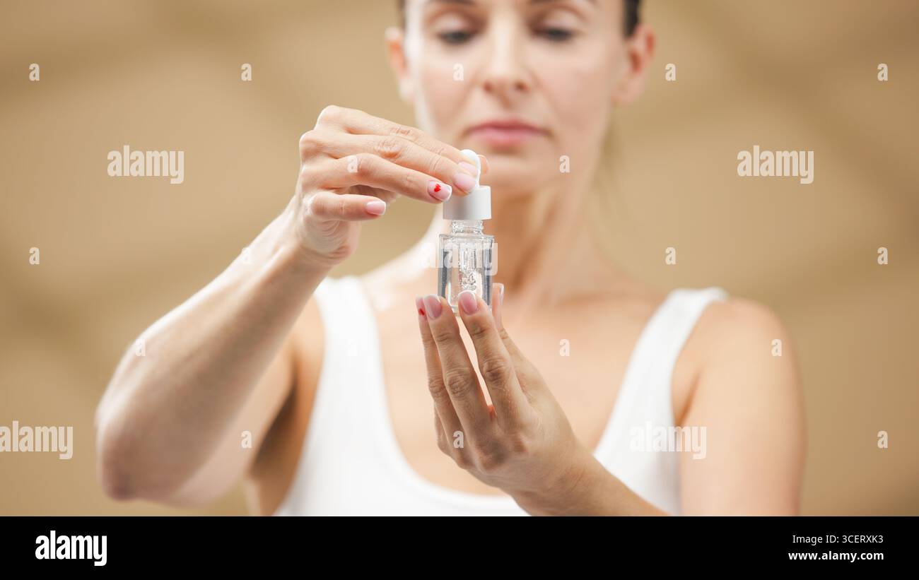 Una donna concentrata sta applicando delicatamente il siero da un flacone contagocce, evidenziando la sua routine di cura della pelle in un ambiente tranquillo, promuovendo benessere e benessere Foto Stock