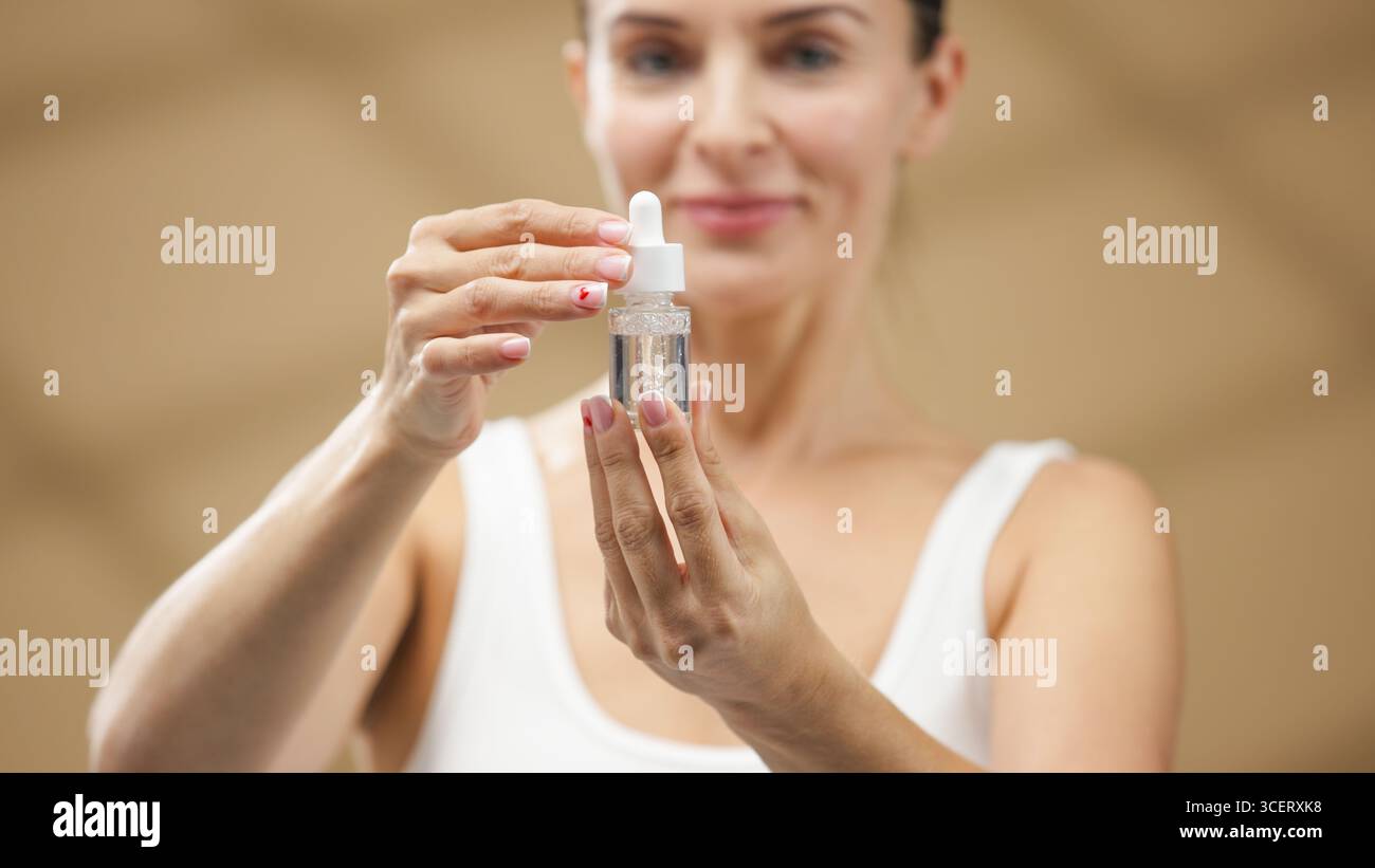 La modella femminile tiene in mano un flacone contagocce di siero, dimostrando un prodotto per la cura della pelle in un ambiente benessere sereno, circondato da luci soffuse e n Foto Stock