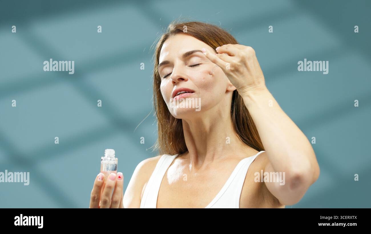 La modella femminile applica delicatamente il siero facciale con un contagocce, evidenziando un rituale lenitivo per la cura della pelle in un ambiente tranquillo e benessere, concentrandosi sull'idr Foto Stock