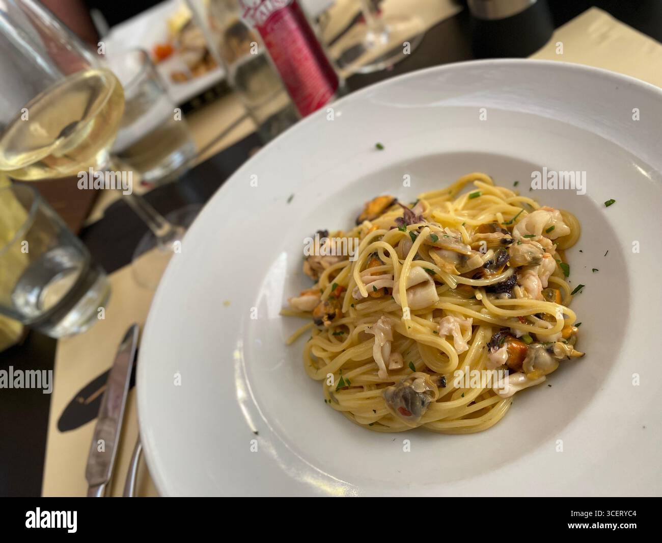 Pasta con salsa all'olio d'oliva e vongole fresche con un bicchiere di vino bianco Foto Stock