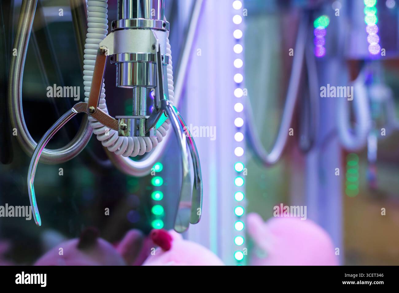 Primo piano di un artiglio in una sala giochi, con vivaci luci LED e peluche a portata di mano, per creare un'atmosfera di gioco emozionante. Foto Stock