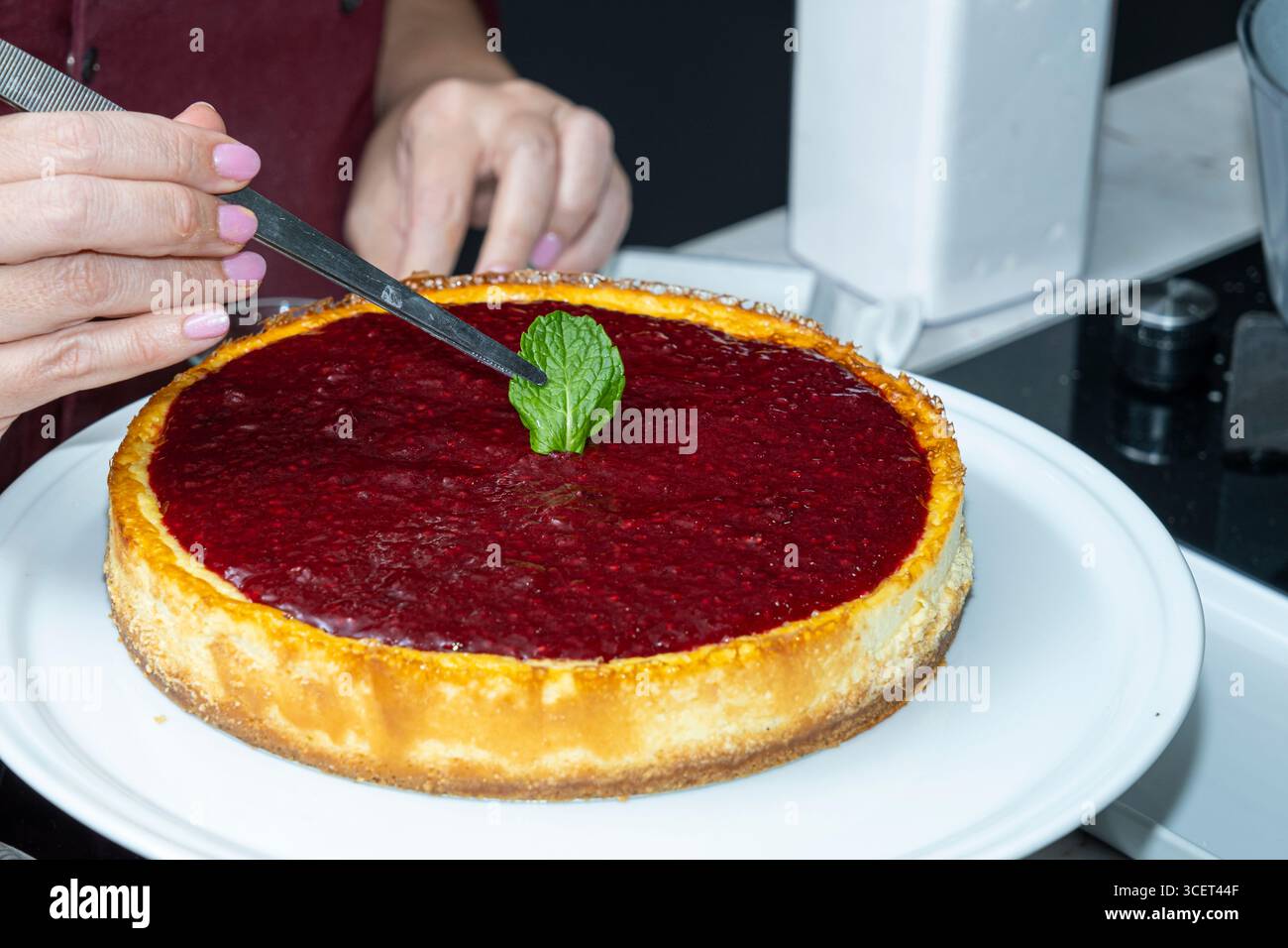 Lo chef posiziona una foglia di menta sulla cheesecake con una salsa di frutti di bosco. Foto Stock