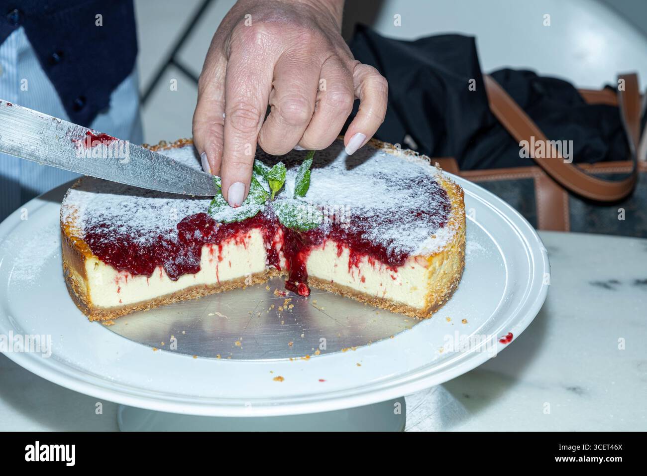 Donna che affetta cheesecake con marmellata di frutti di bosco. Foto Stock
