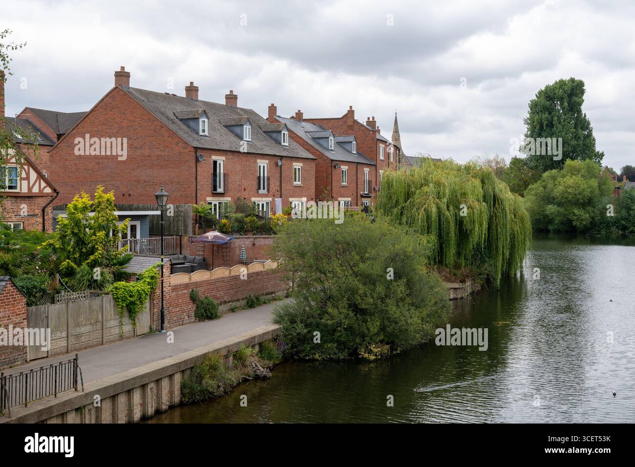 Fila di case in mattoni rossi lungo il fiume con vegetazione urbana fornita da alberi vicini. Foto Stock